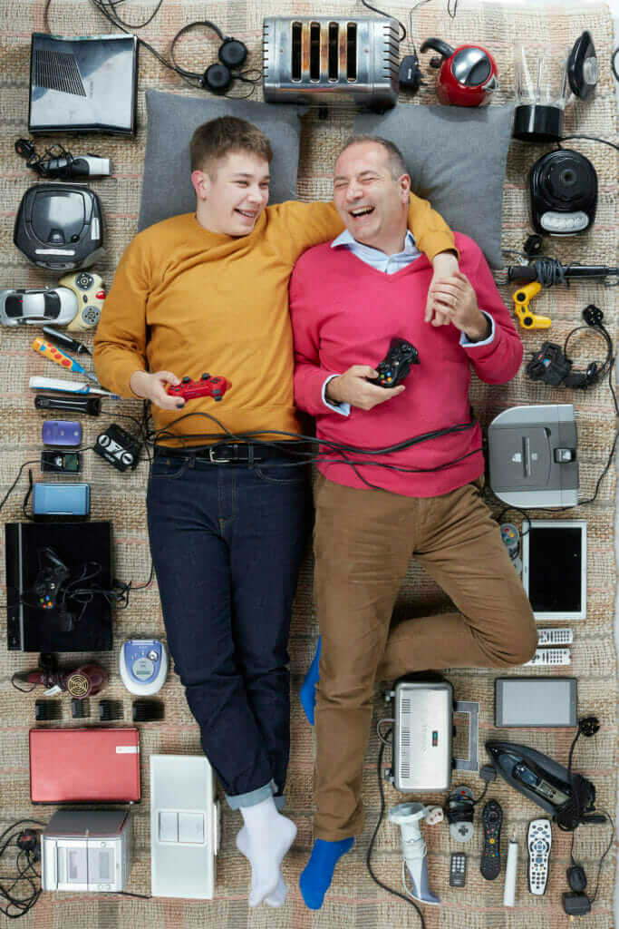 overhead shot of A light skinned man and a boy lying down amongst a lot of electrical goods while laughing