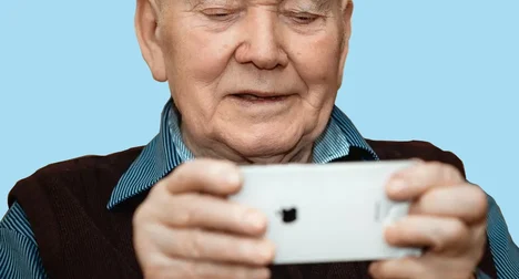 Pale skinned older man holding a mobile phone in front of his face